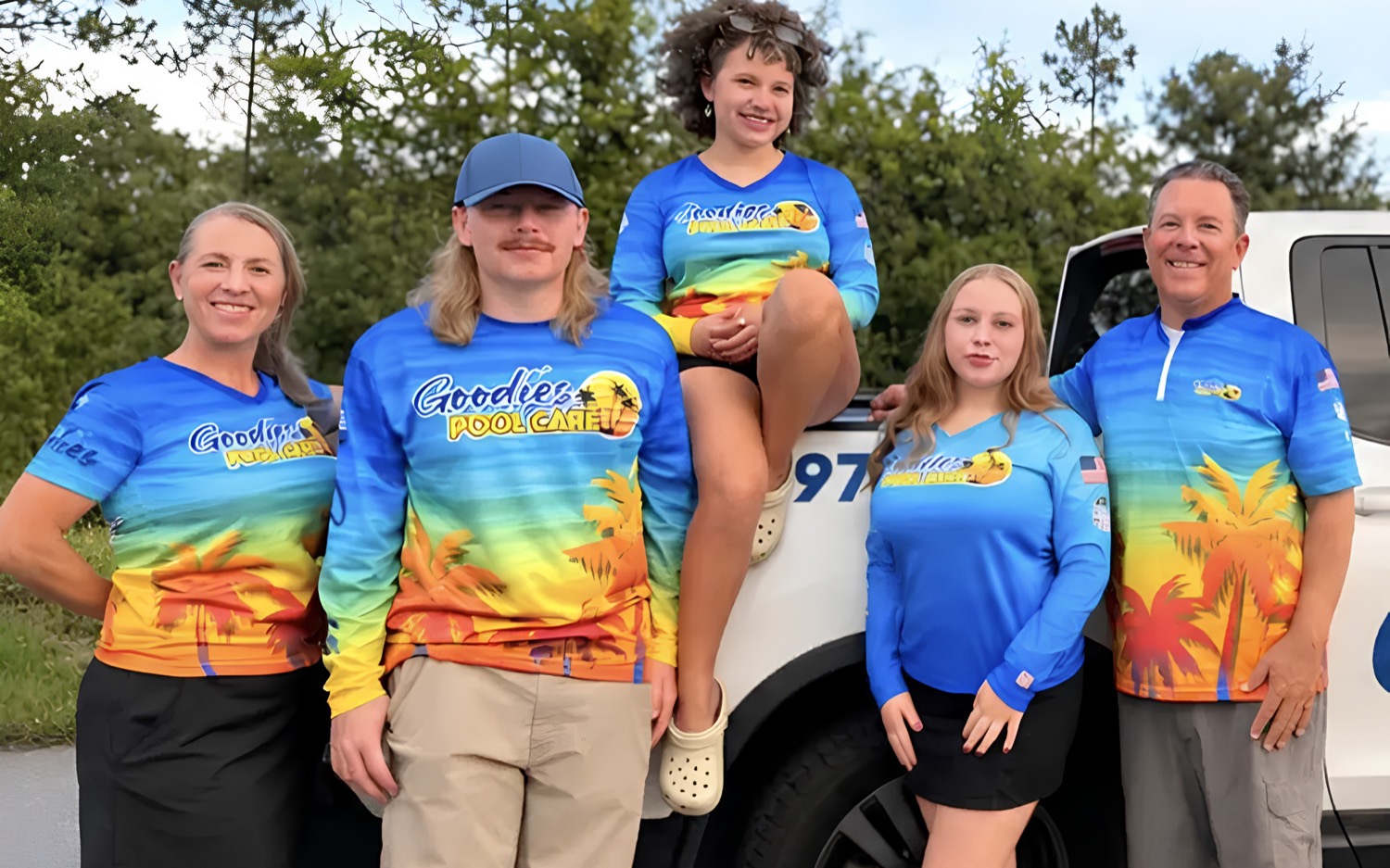 The Goodies Pool Care family in matching sunset shirts beside their wrapped white pickup truck in Bay County, Florida