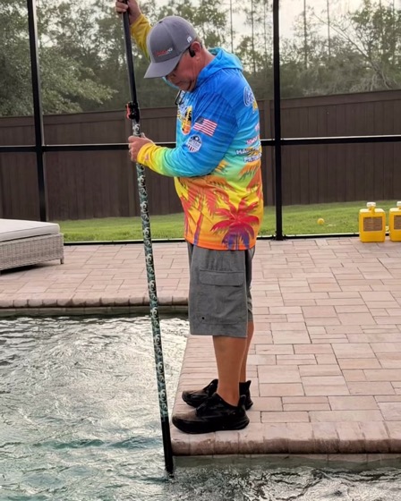 A Goodies Pool Care technician brushing the walls of a screened pool