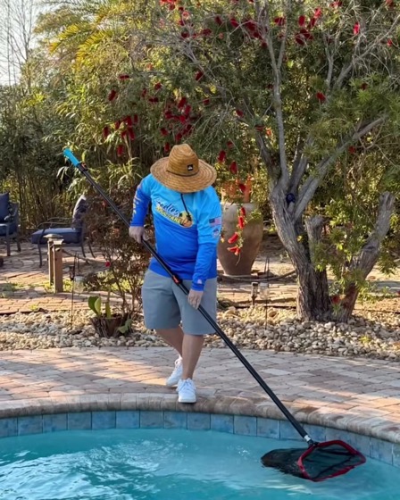 A Goodies family member vacuuming a pool under palms