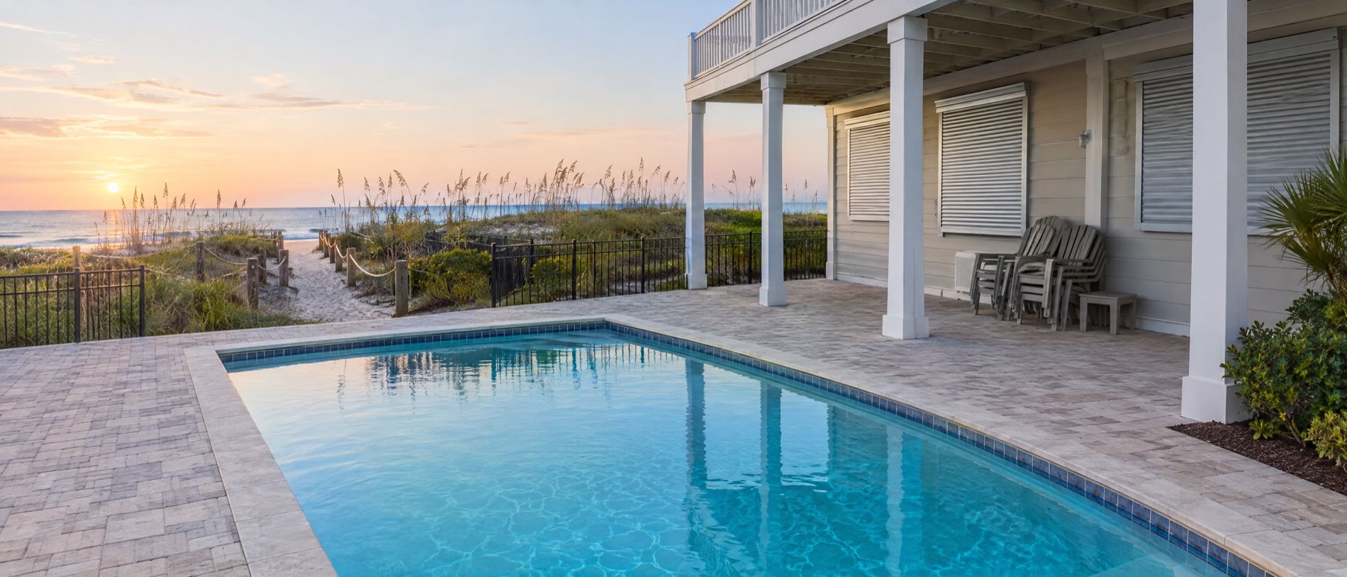 A clean pool behind a shuttered beach house in Panama City Beach, with the patio chairs stacked while the owners are away