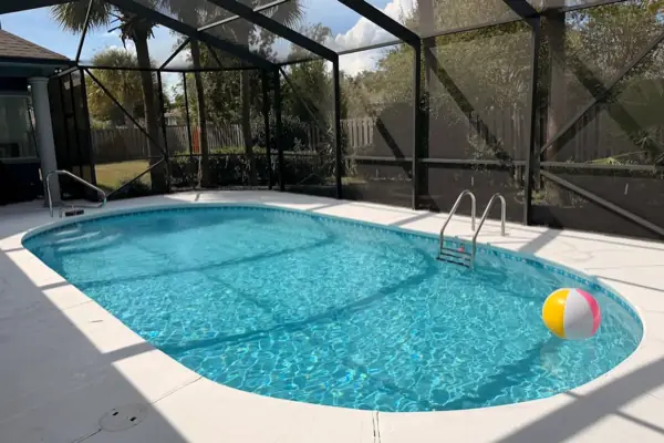 A clear oval pool inside a screen enclosure, with a beach ball floating in the water