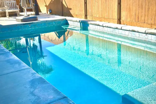 Clear blue water along the tile line of a rectangular pool beside a wooden fence
