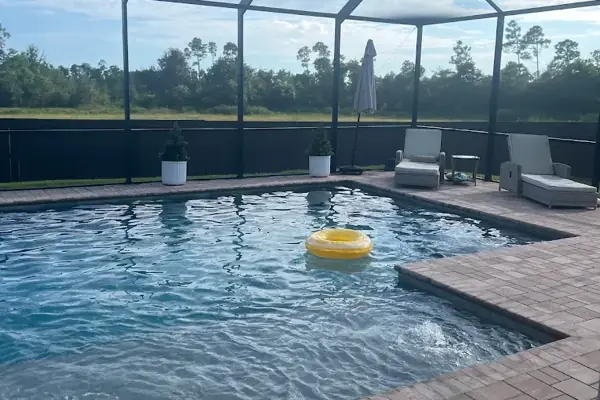 A screened pool with a paver deck, patio chairs and a yellow float on the water