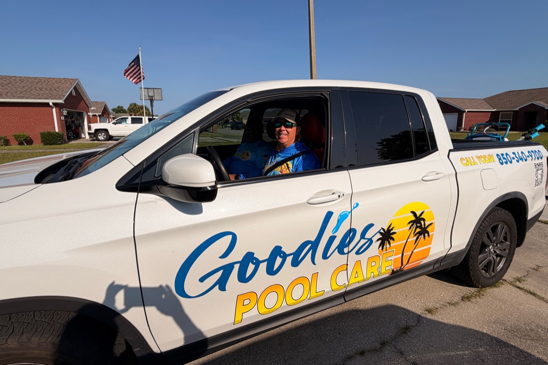 A Goodies Pool Care technician smiling from the driver’s seat of the company truck, the Goodies Pool Care logo on the door